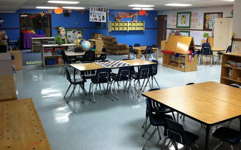 Empty classroom with multiple tables, chairs, and learning materials