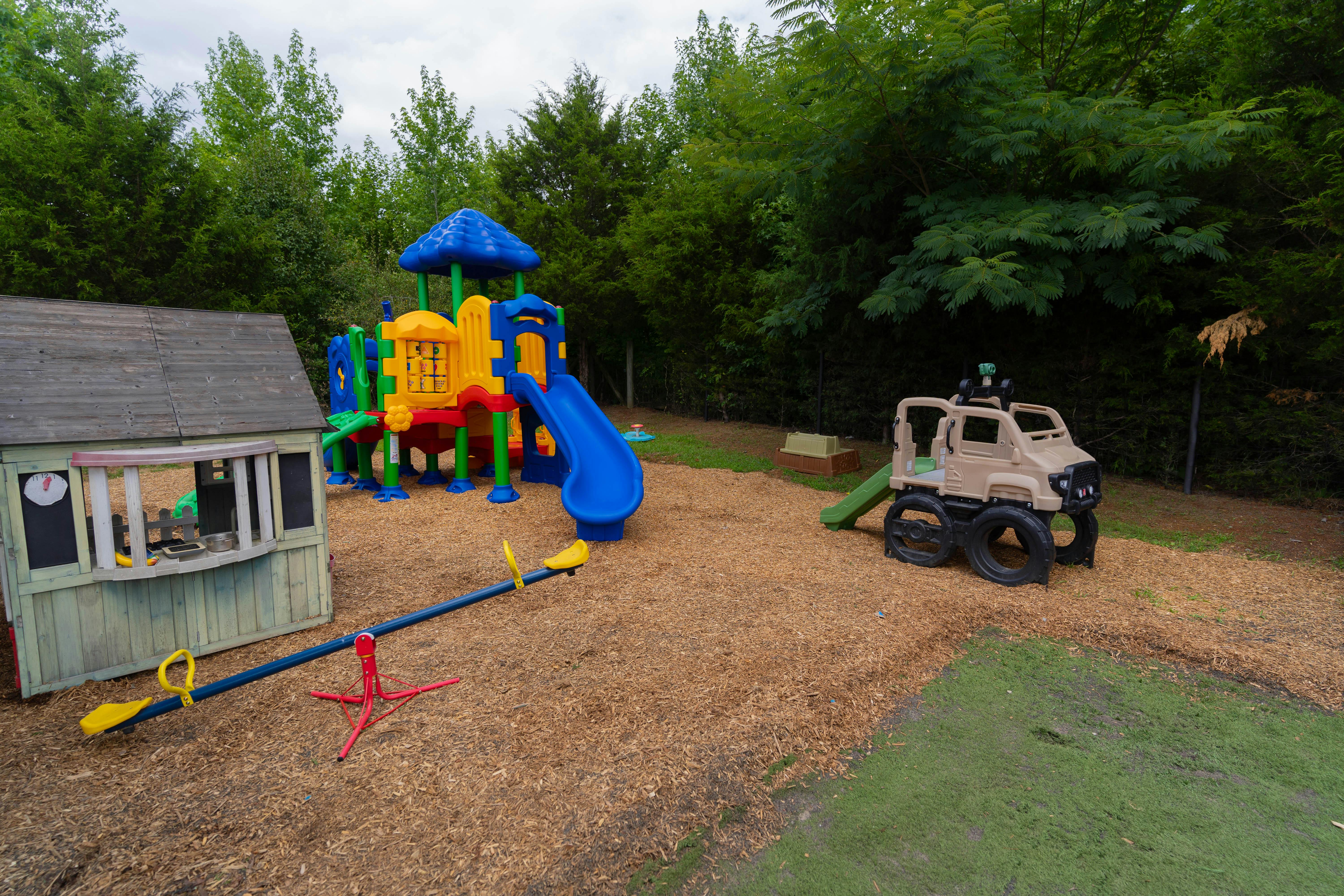 Playground with playhouse, colorful slide structure, seesaw, and toy truck