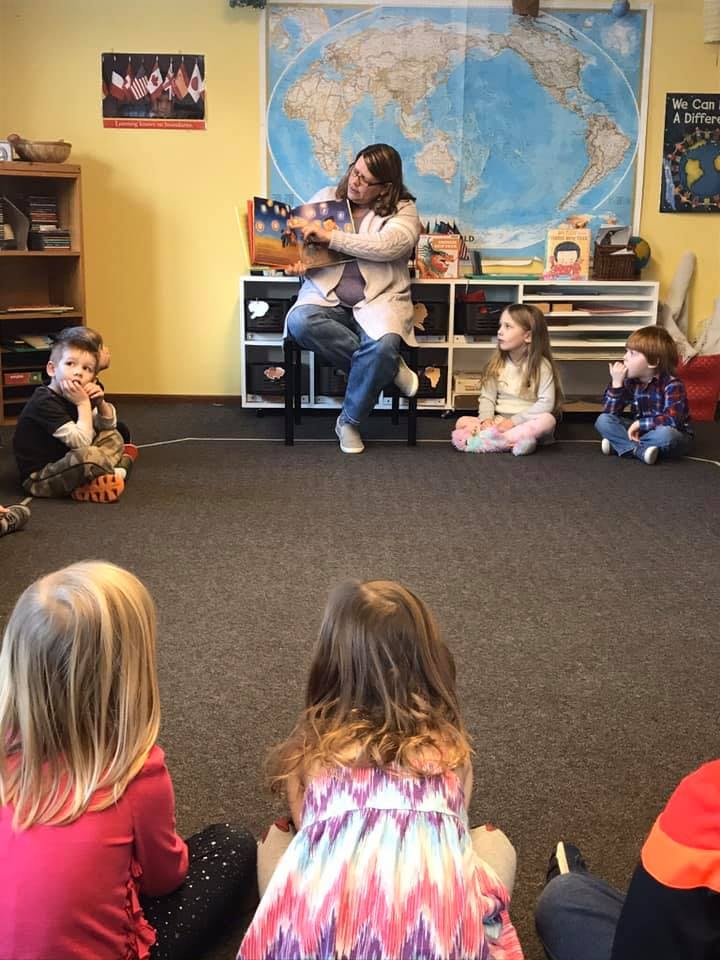 Adult reading a book to children sitting on the floor in a classroom