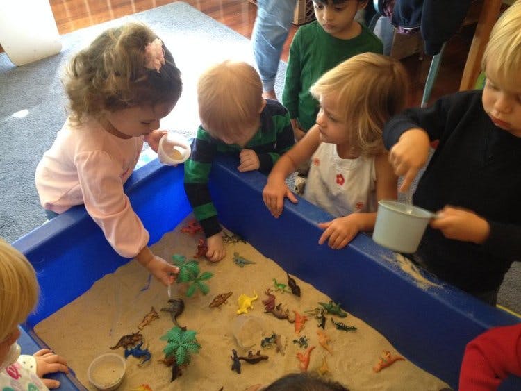 Children playing in a sand table with toy animals
