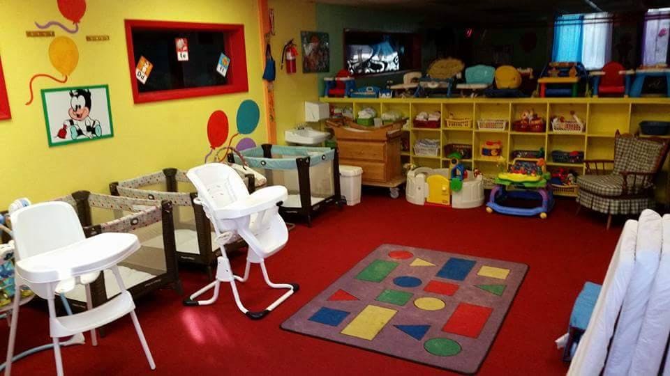 Childcare room with cribs, high chairs, and a colorful rug