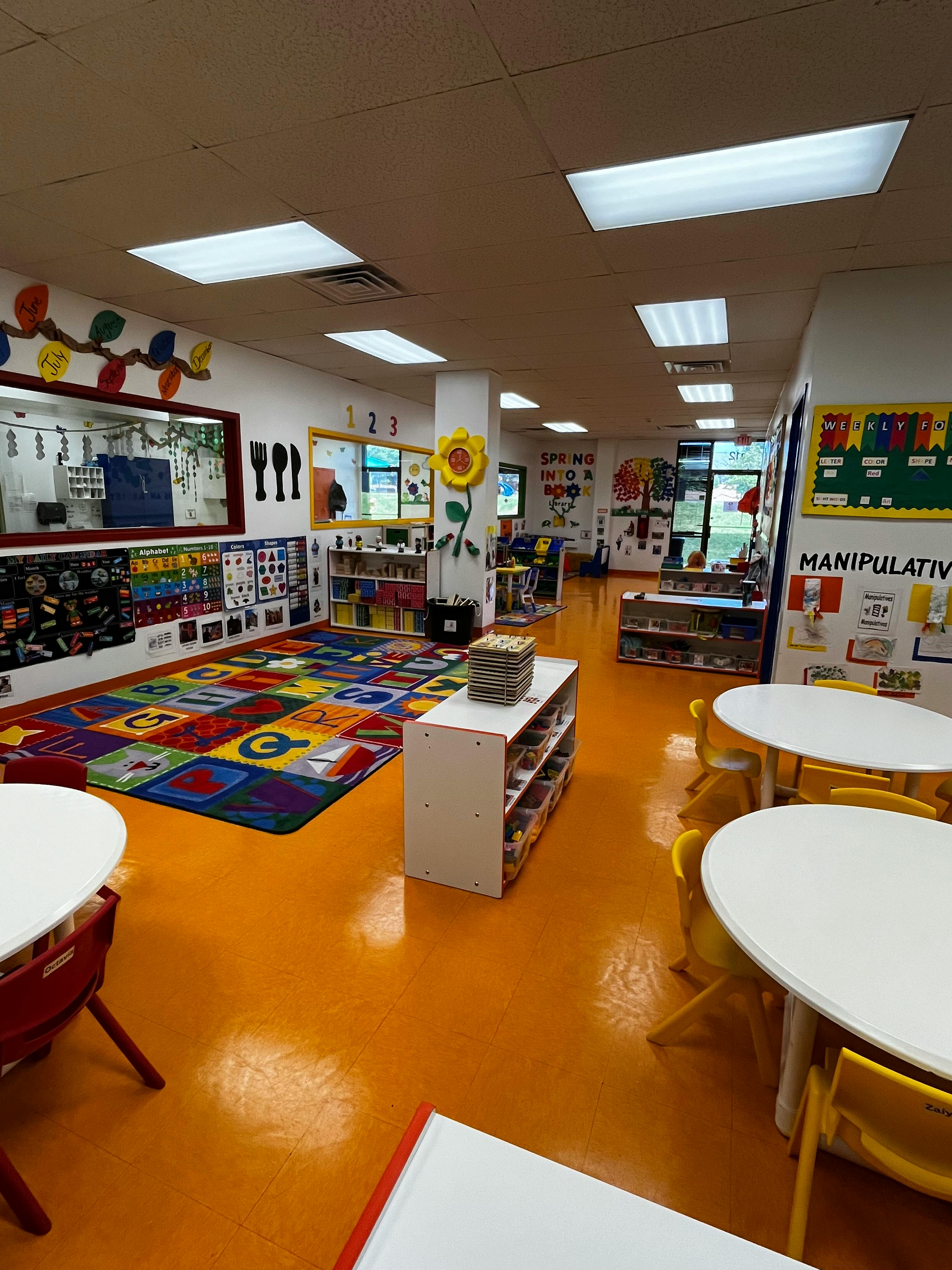 Empty classroom with colorful rug, tables, and shelves