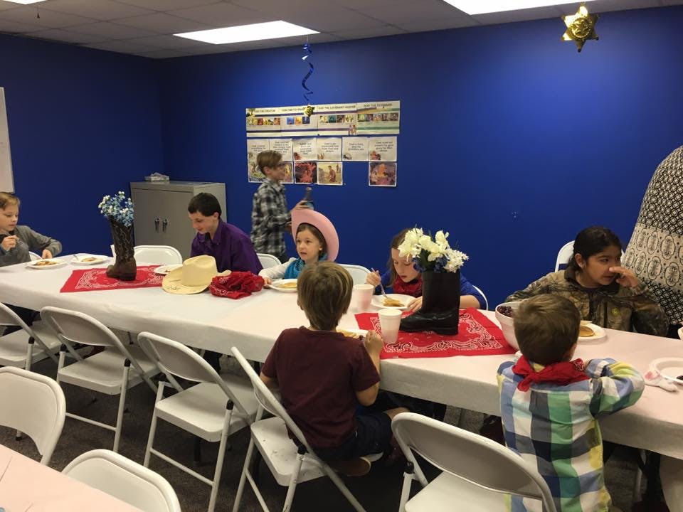 Children and adults seated at a long table with food and drinks