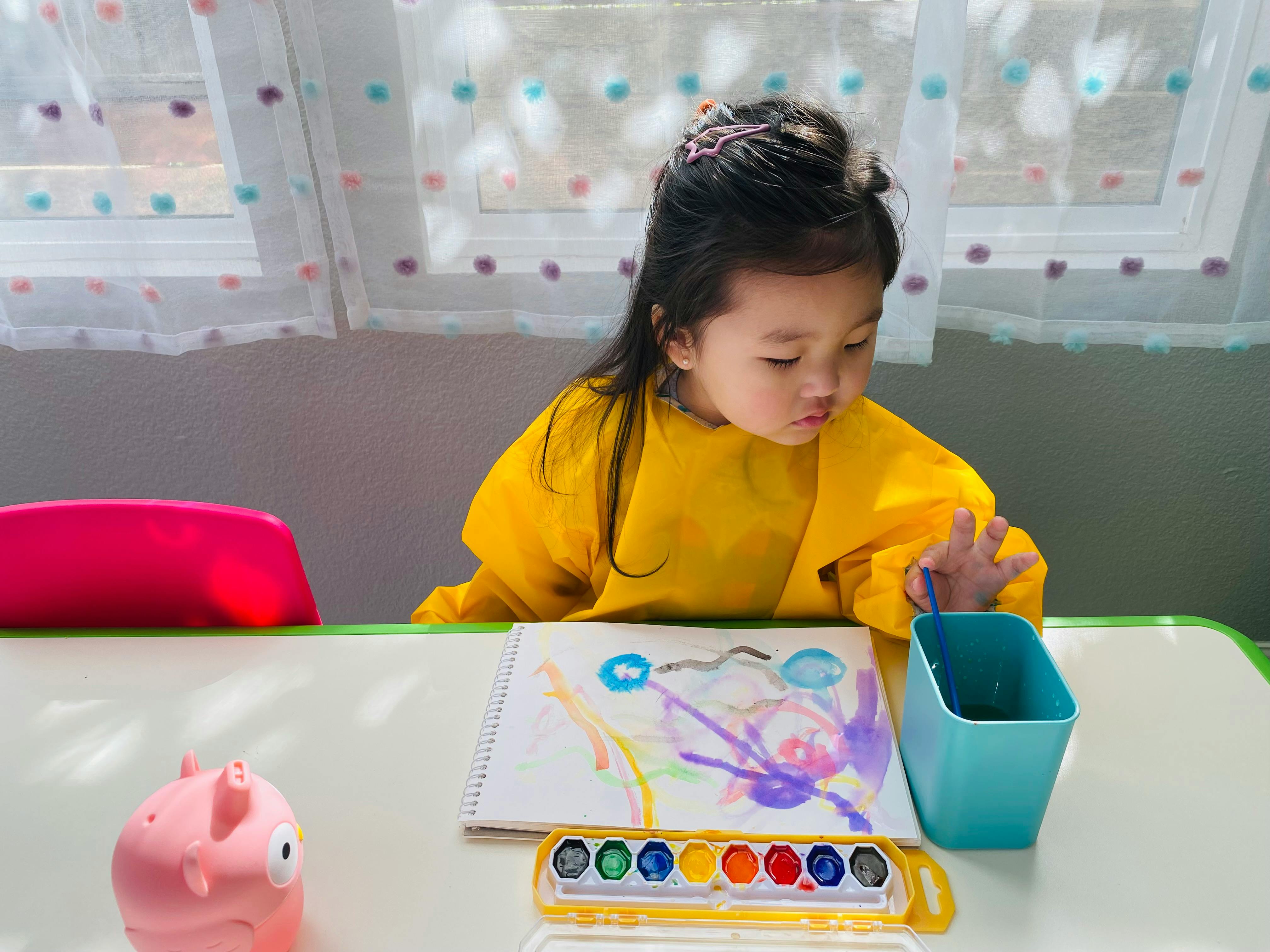 Child in a yellow smock painting with watercolors at a table