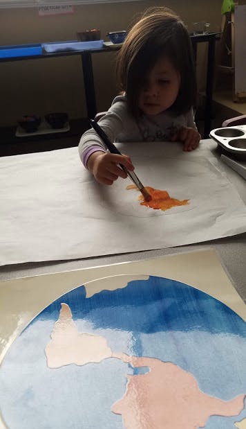 Child painting on paper with orange paint