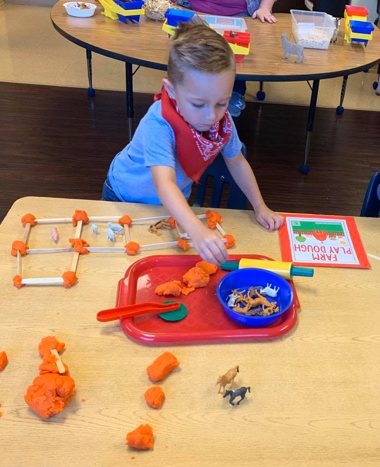 Child playing with orange playdough and animal figurines at a table
