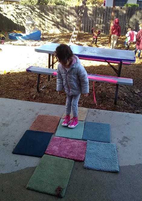 Child standing on colorful mats on concrete