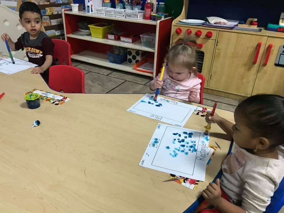 Three children painting at a table in a classroom