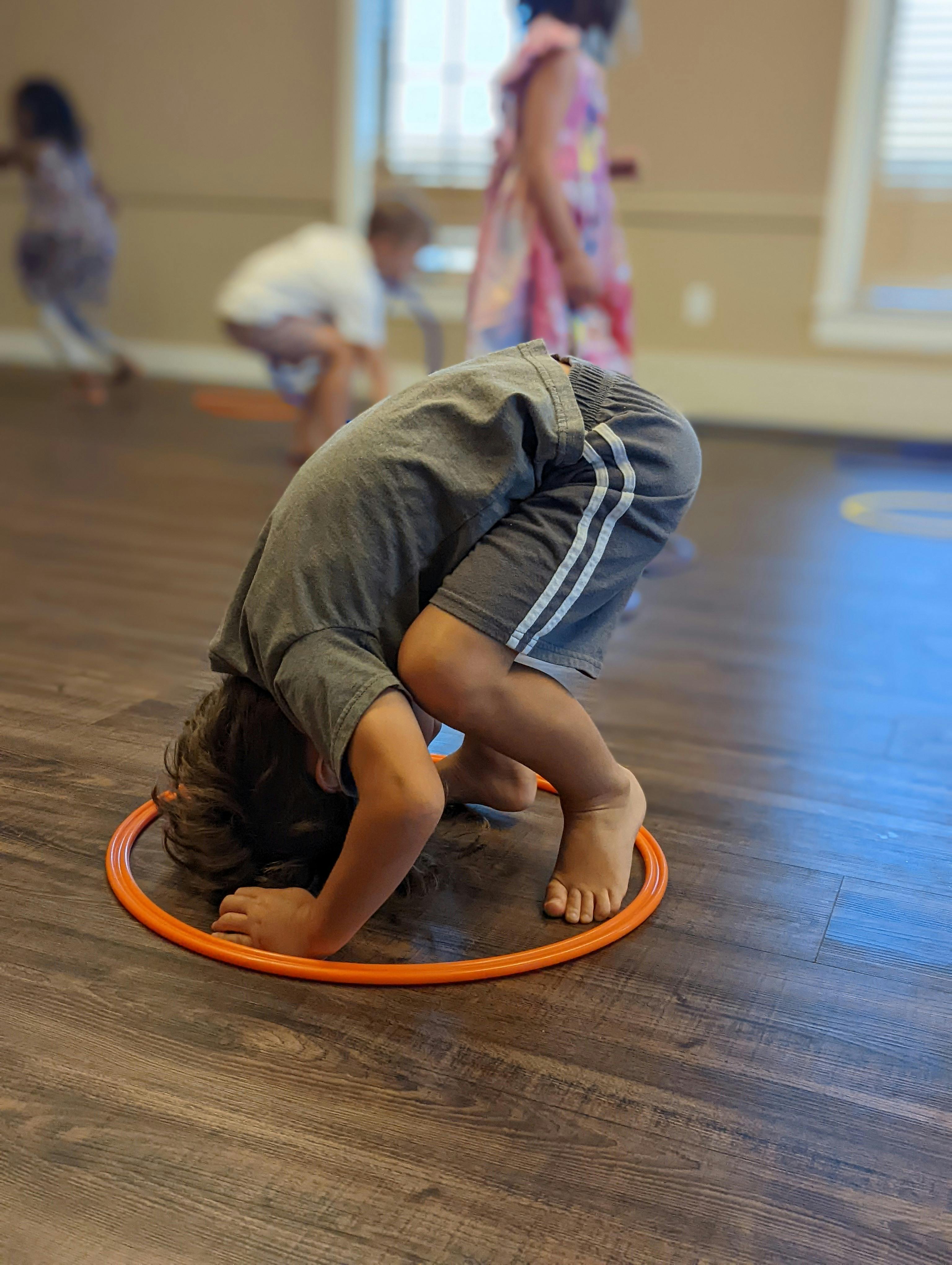 Child bending over with head near an orange hoop on the floor