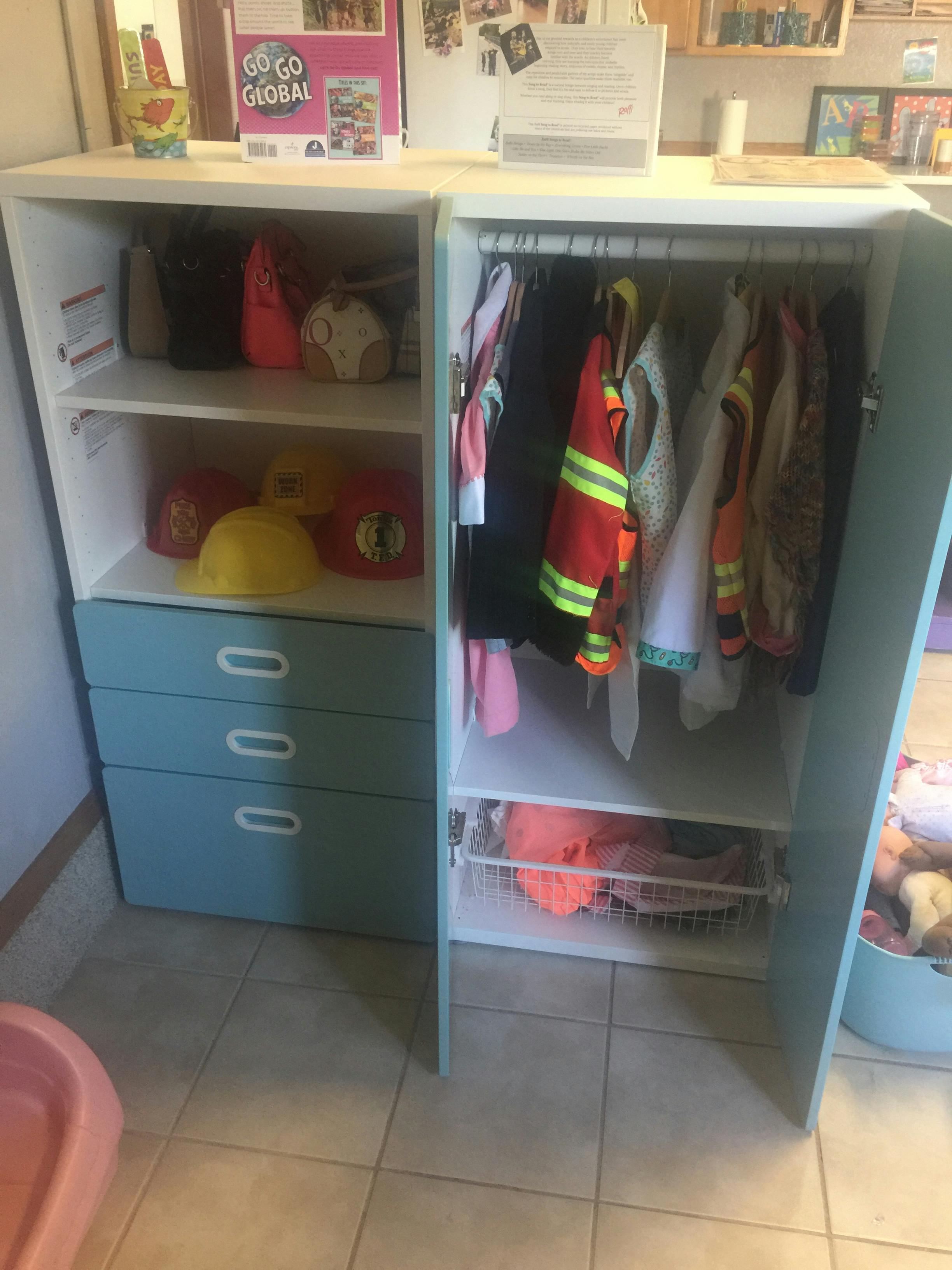 Children's costumes, bags, and toys in an open storage unit with blue drawers