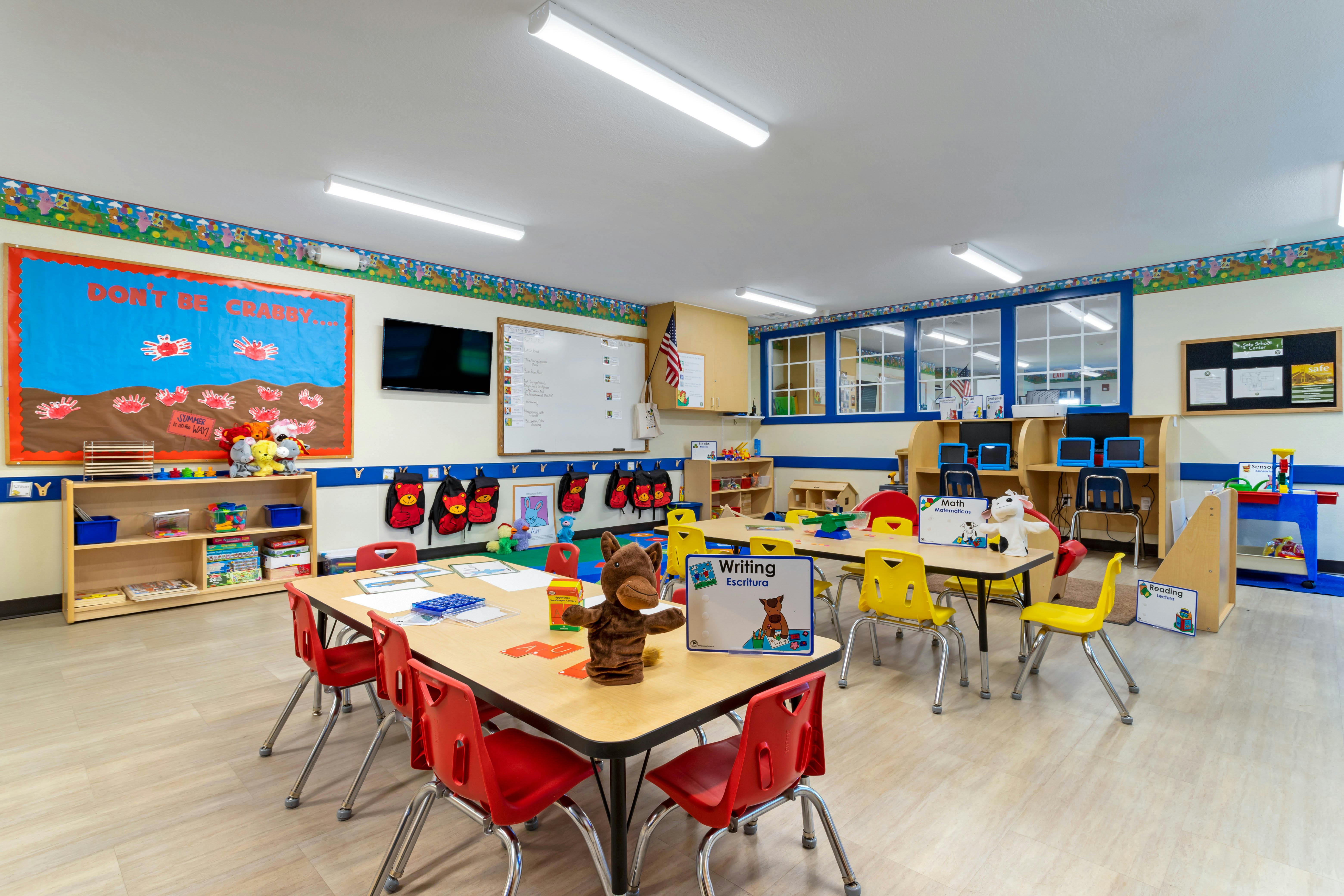 An empty classroom with several small tables and chairs, toys, and learning materials