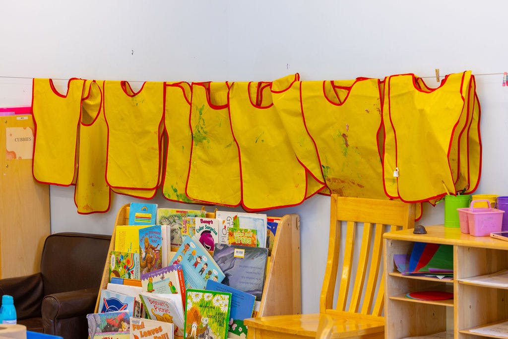 Yellow art smocks hanging above a bookshelf in a classroom