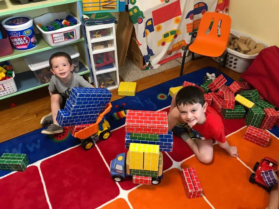 Two children playing with toy trucks and blocks on a colorful rug