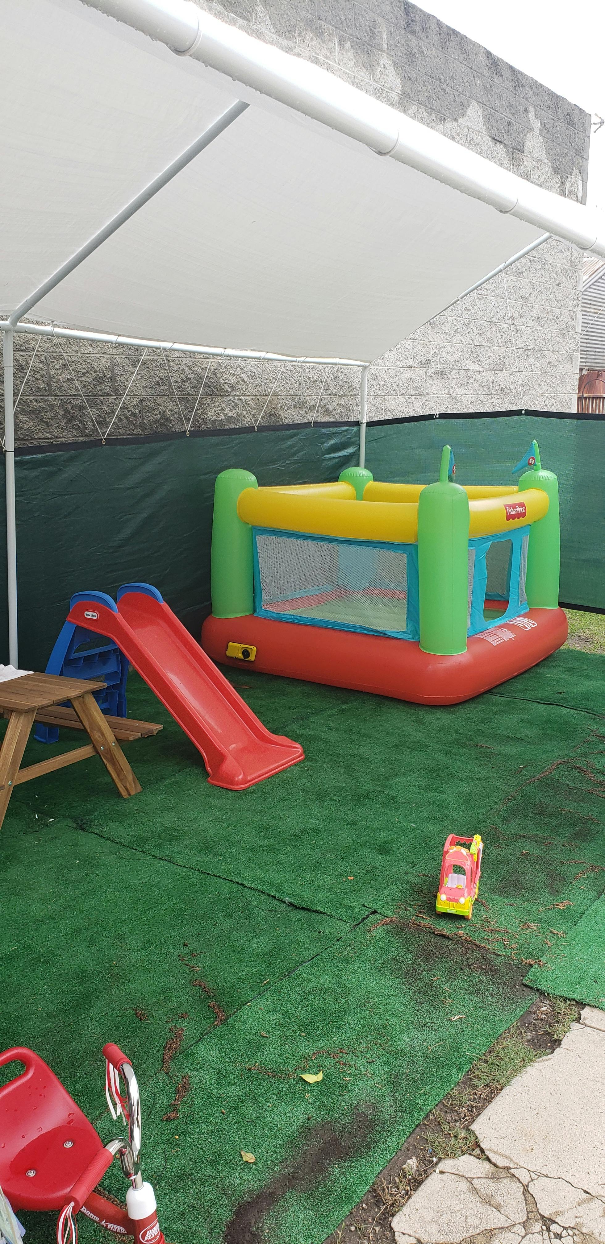 Inflatable bounce house and red slide on green turf under a canopy