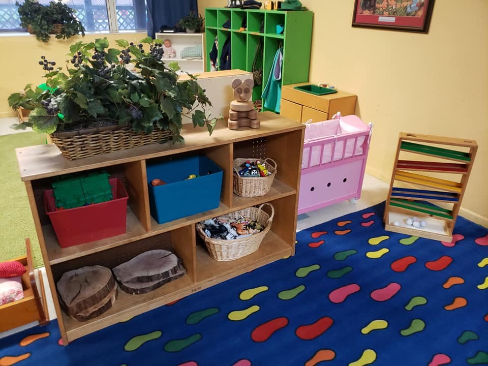 Classroom with colorful rug, wooden shelves, and green cubbies