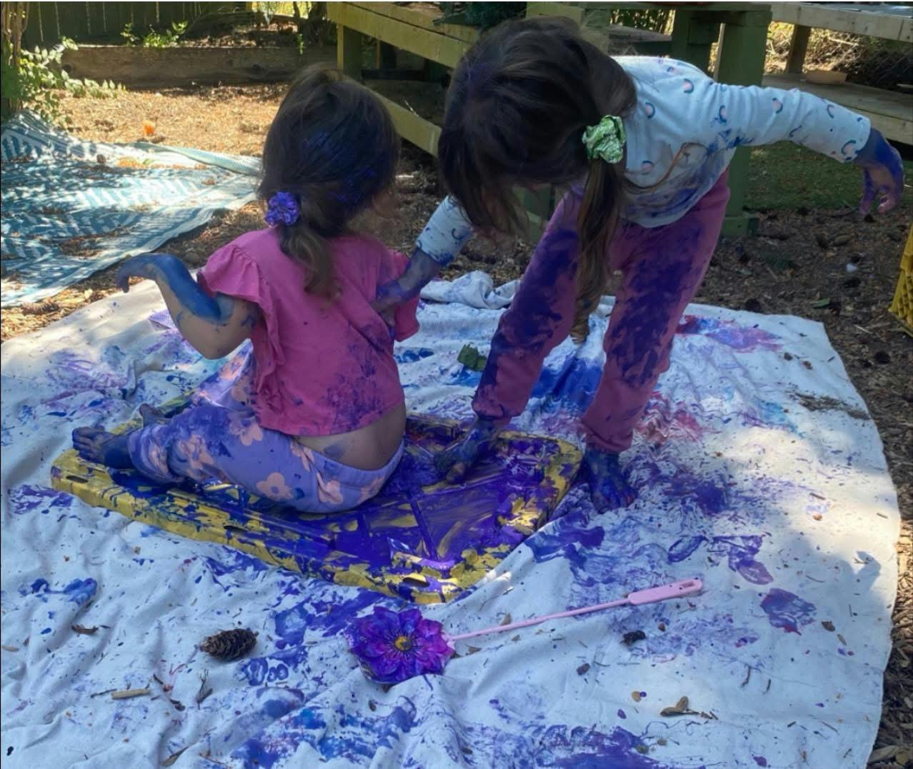 Two children sitting and standing on a cloth covered in purple paint