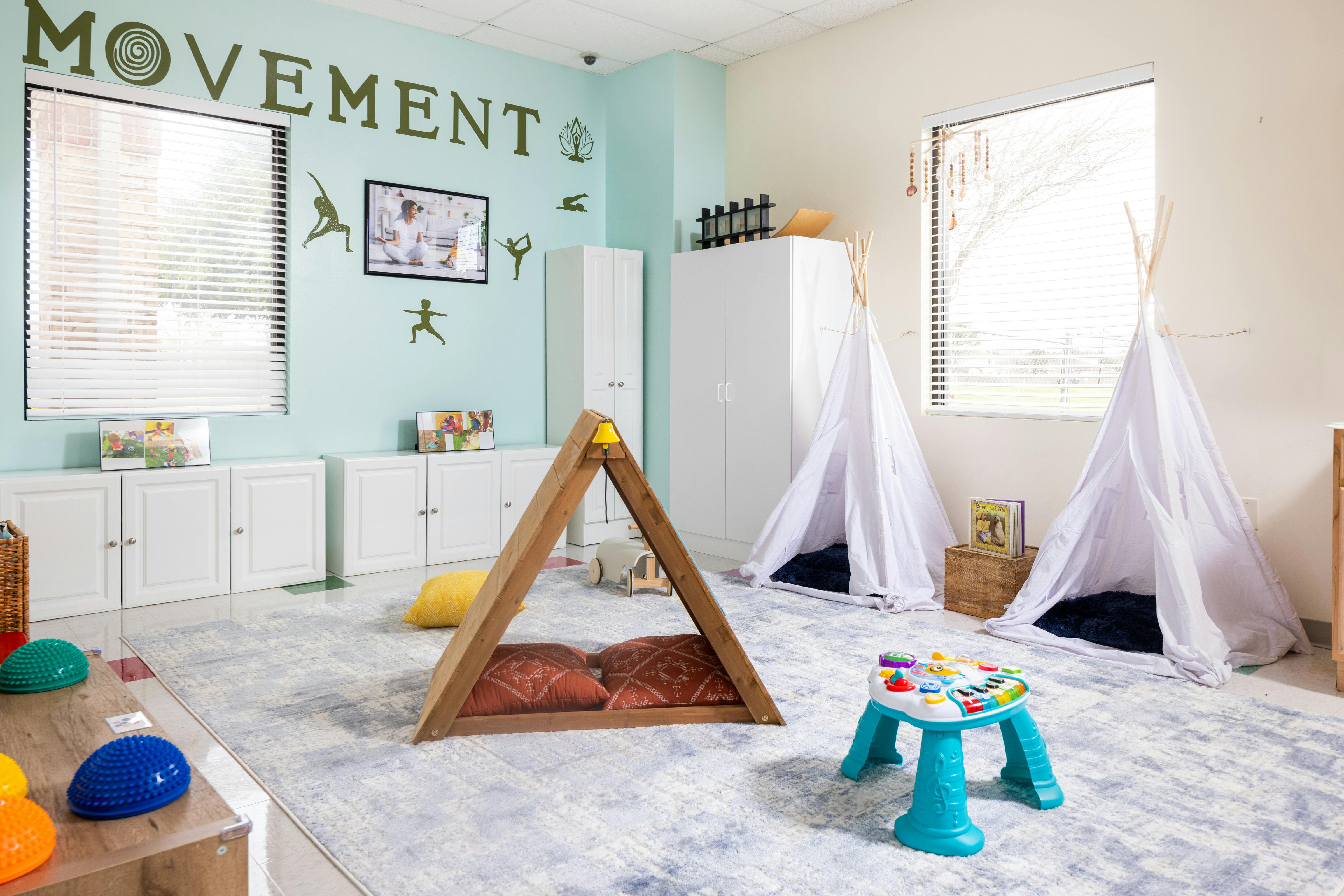Playroom with a wooden A-frame, two white teepees, and a blue activity table
