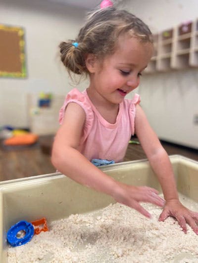Child playing in a sensory bin with hands in a classroom