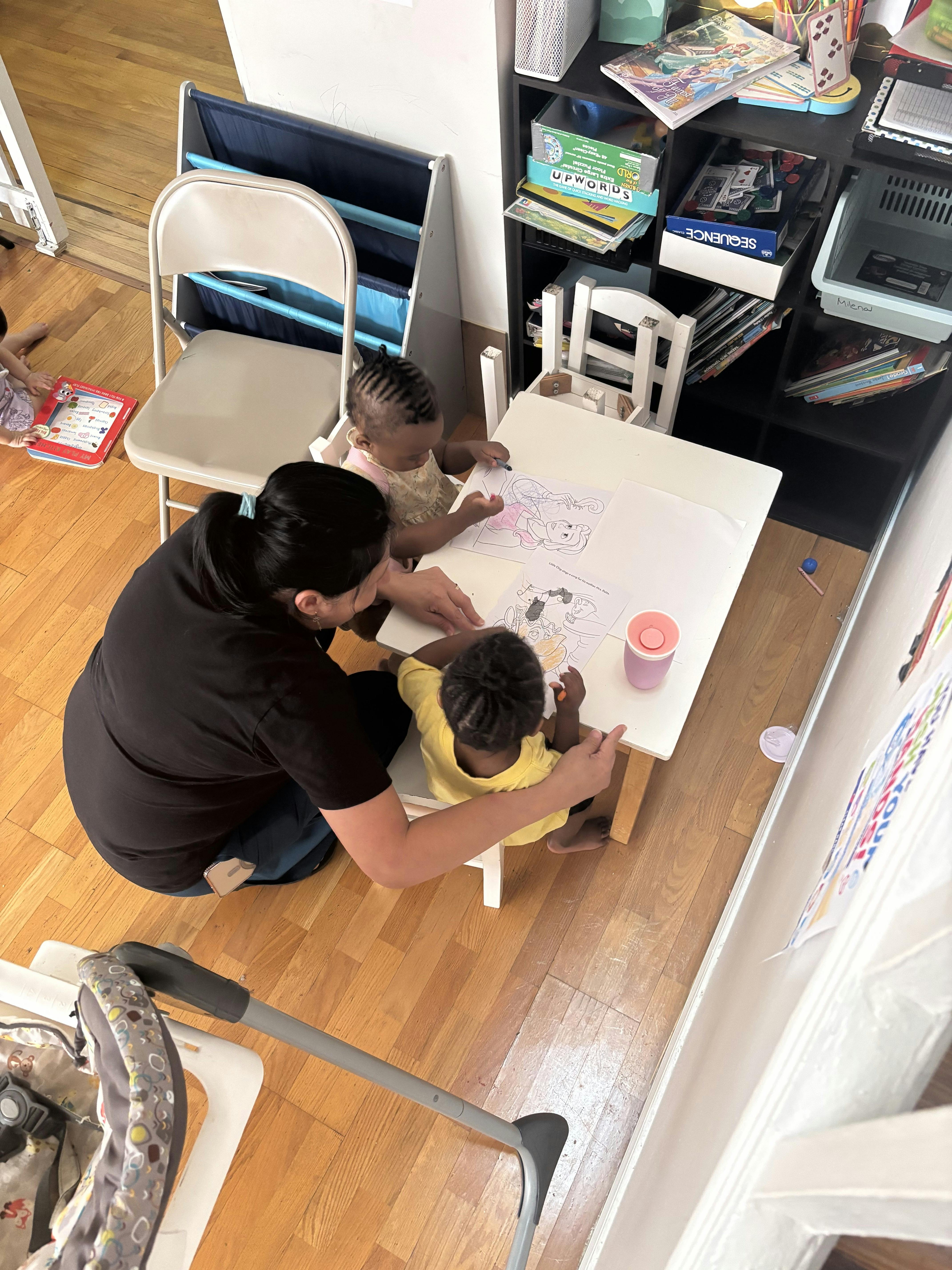 Adult assisting two children with coloring at a small table