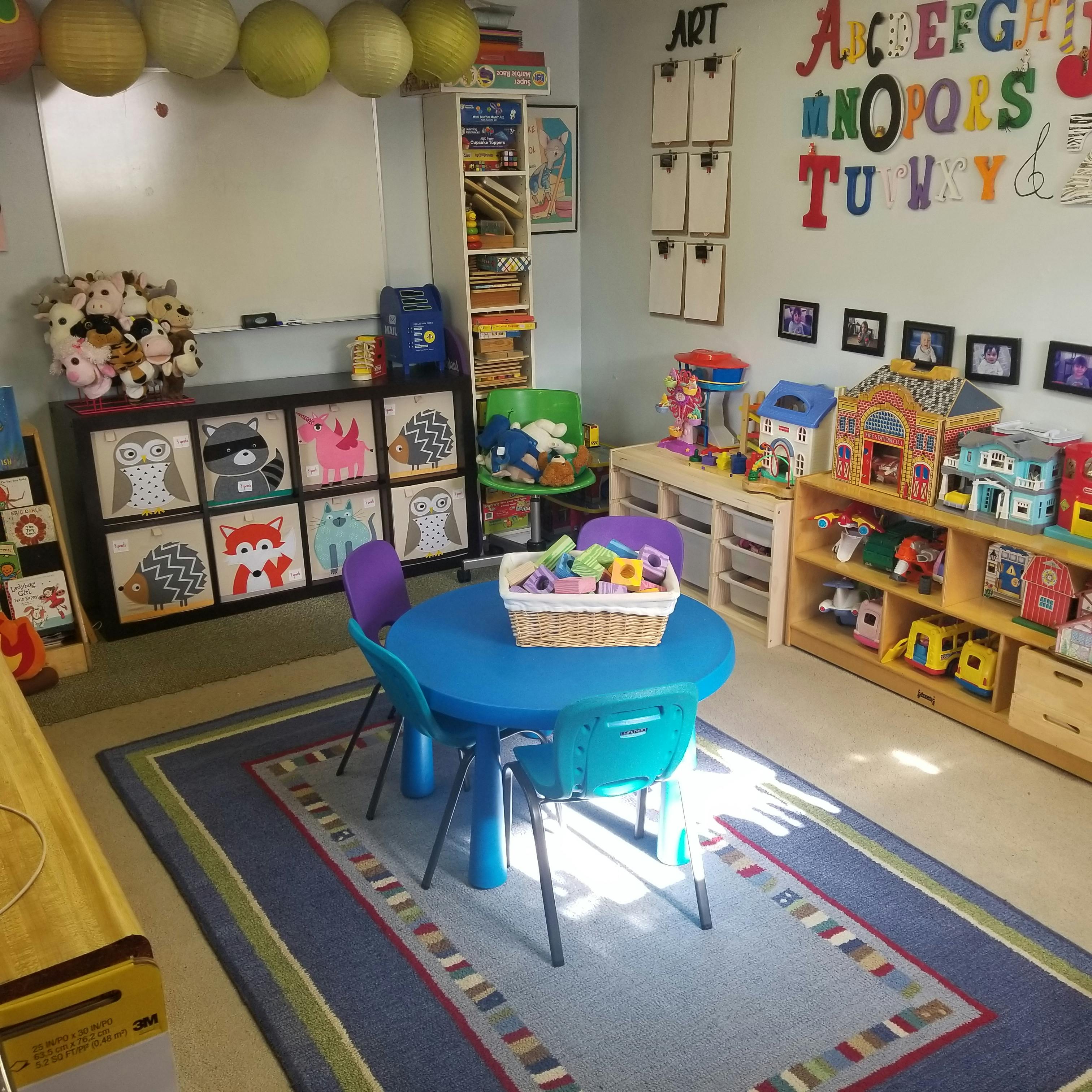 Children's play area with small blue table and chairs, toys, and alphabet on wall