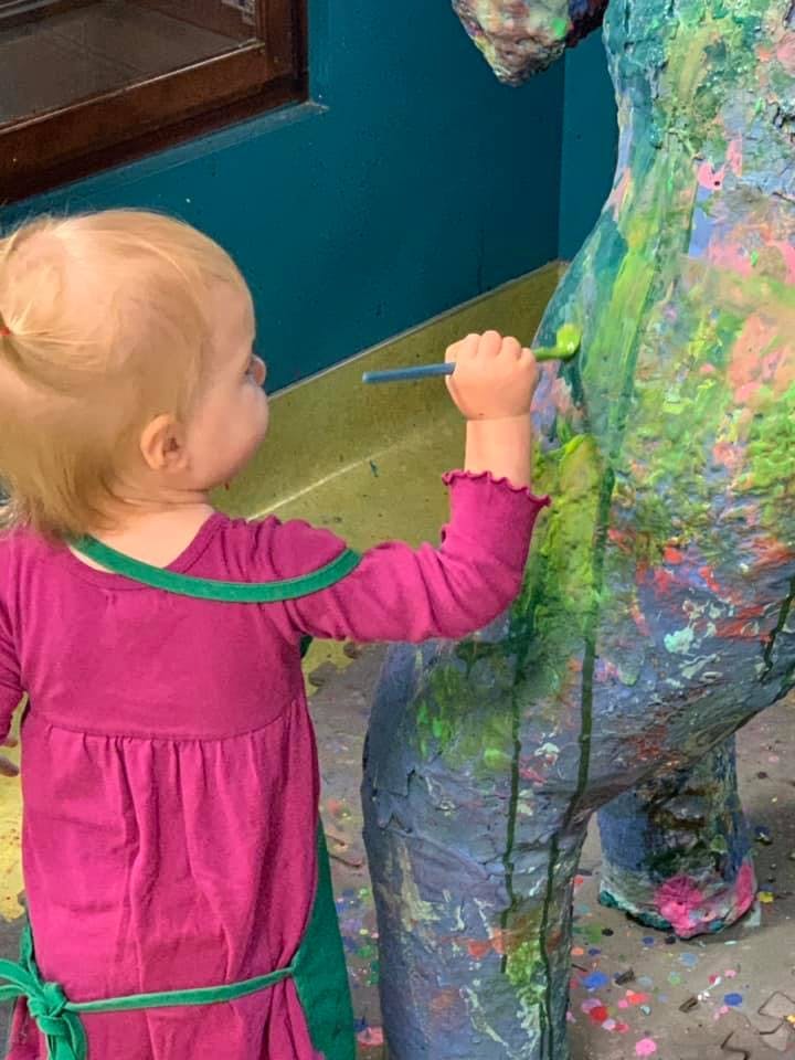 Child in an apron painting a sculpture