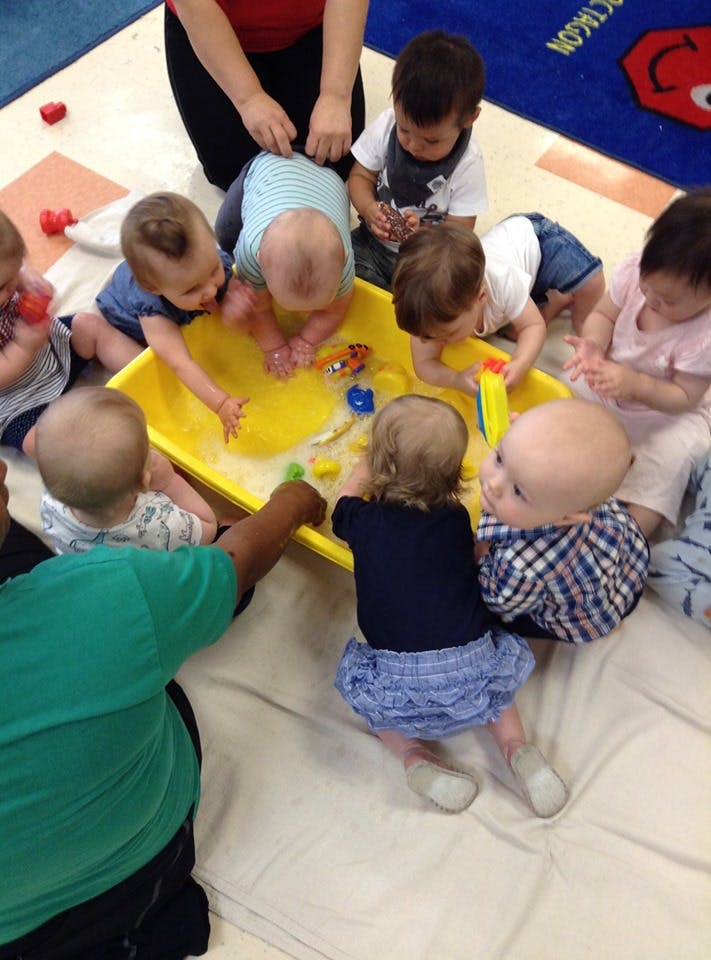 Babies playing in a yellow sensory bin with water and toys