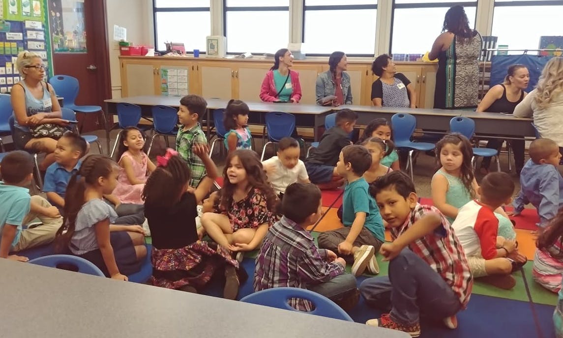 Children and adults sitting on the floor and at desks in a classroom