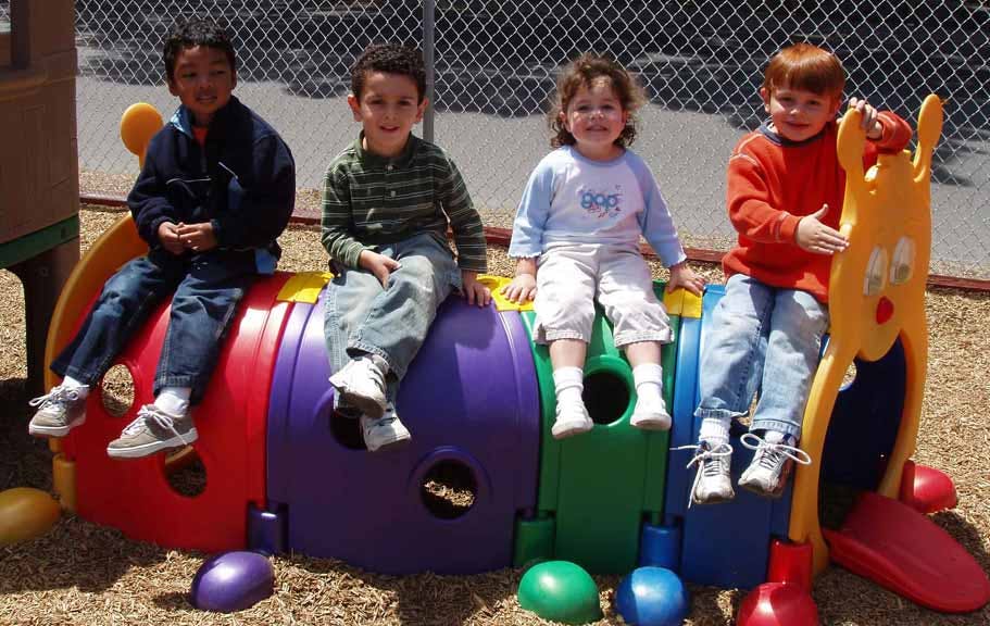 Four children sitting on a colorful playground tunnel