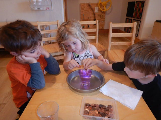Three children at a table with a purple cup in a metal tray