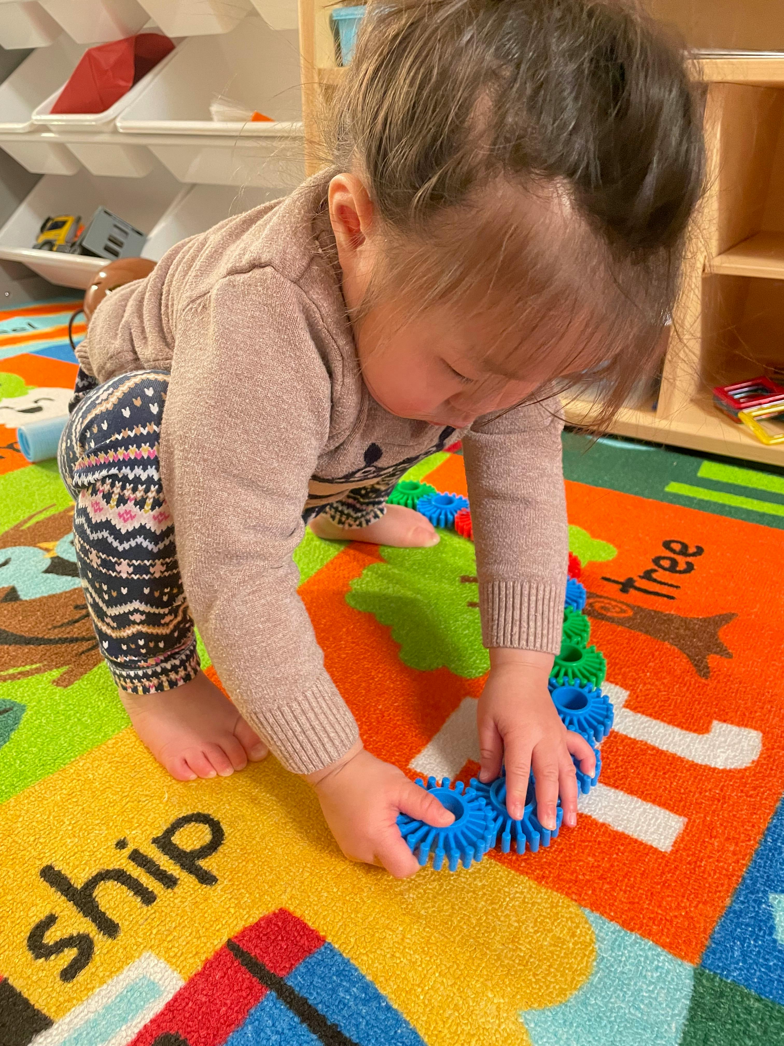 Child playing with blue interlocking toys on a colorful rug