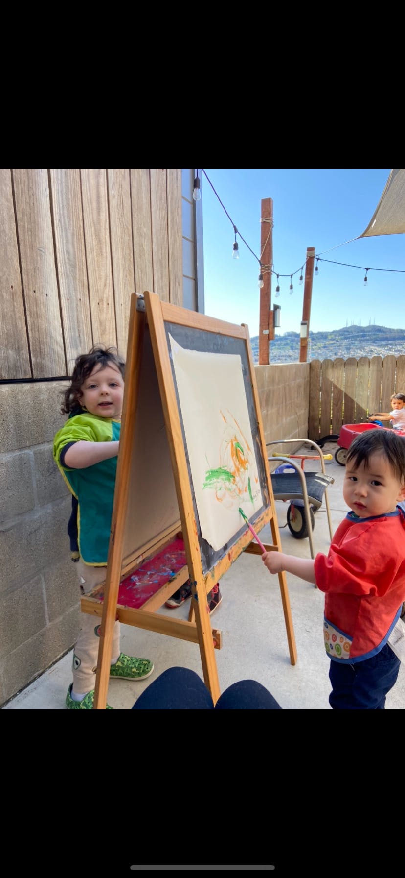 Two children painting at an easel outdoors