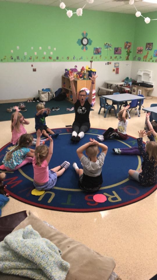 Adult and children sitting in a circle on a rug in a classroom