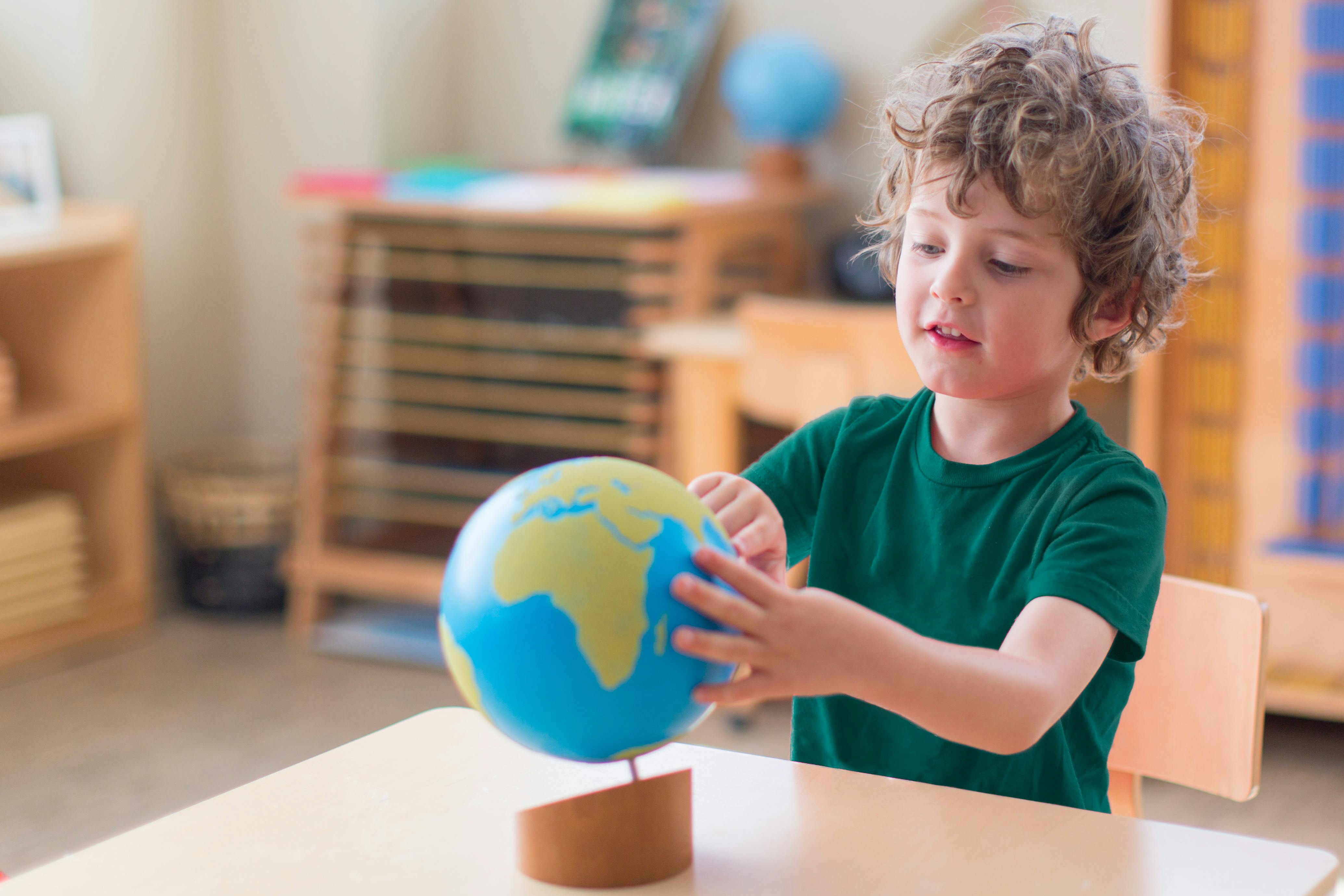 Child touching a globe on a table in a classroom