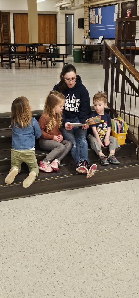 A person reading a book to three children on a staircase