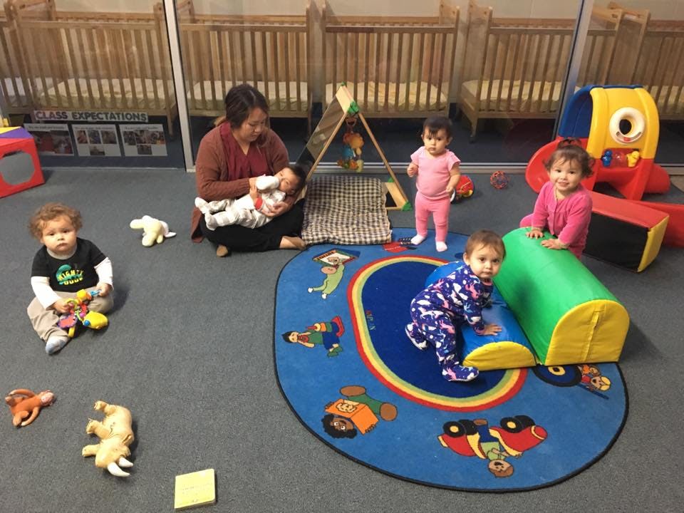 Adult and multiple children playing in a room with cribs in the background