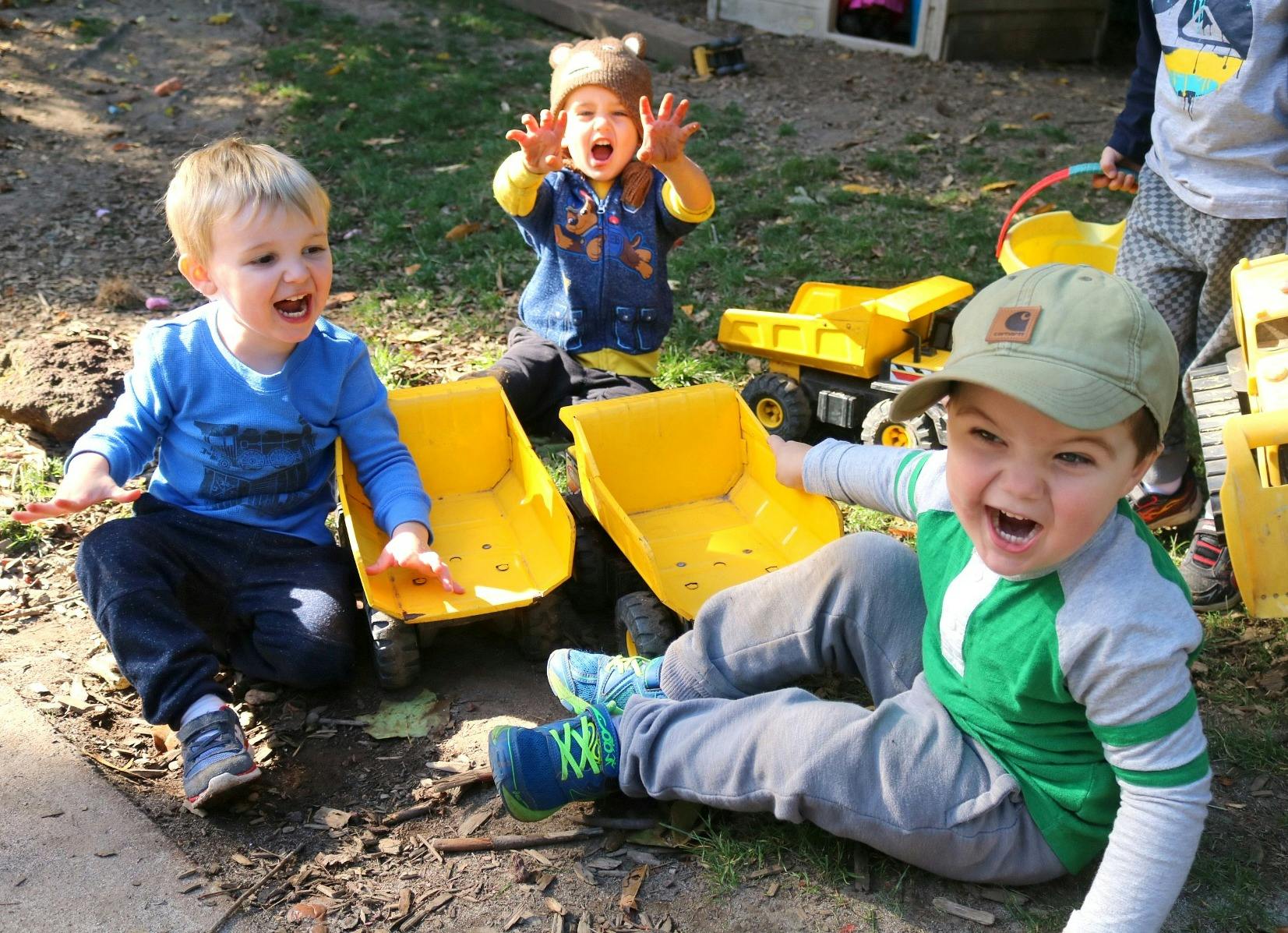 Three children playing outdoors with toy trucks