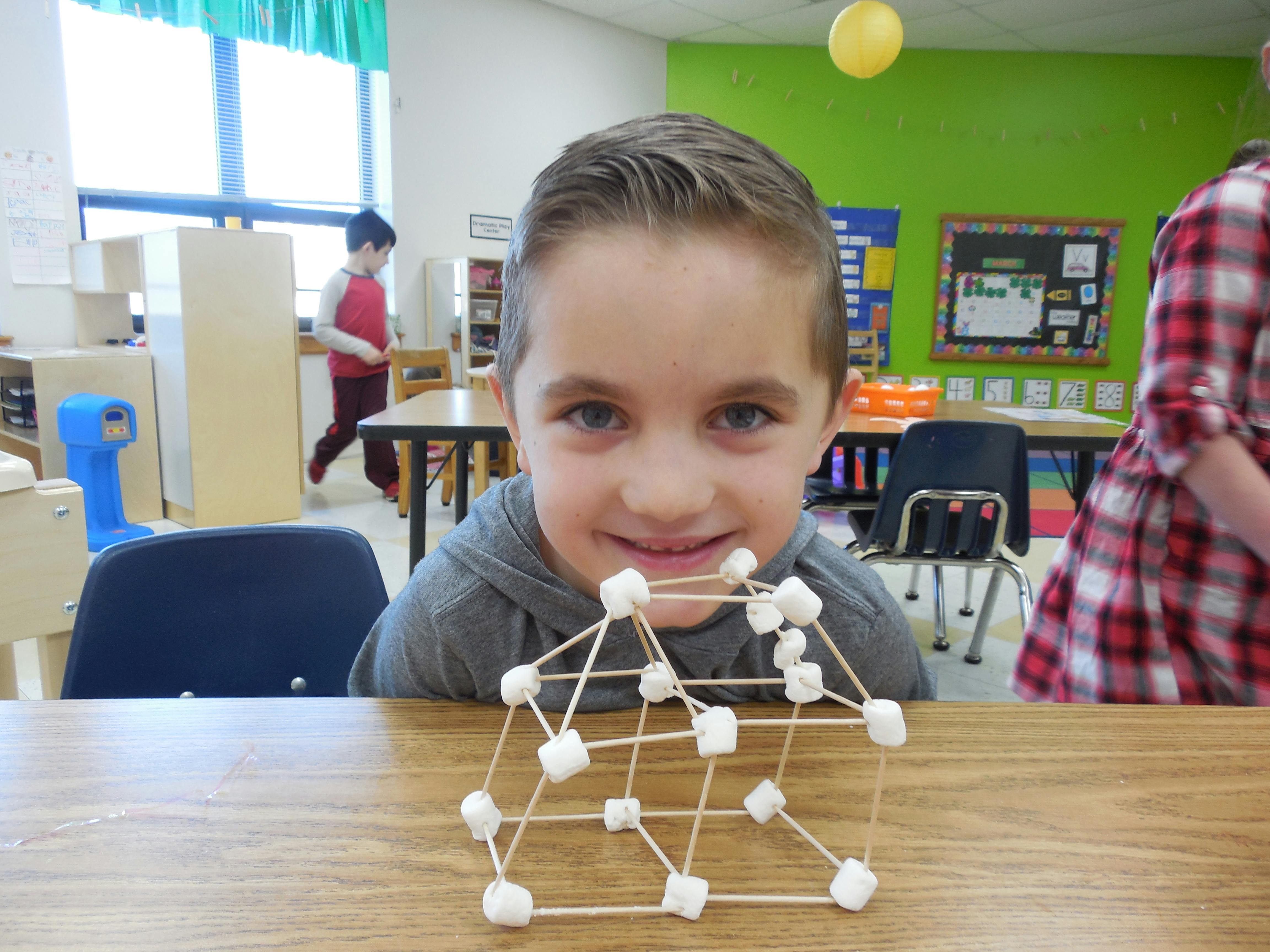 Child with a marshmallow and toothpick structure in a classroom