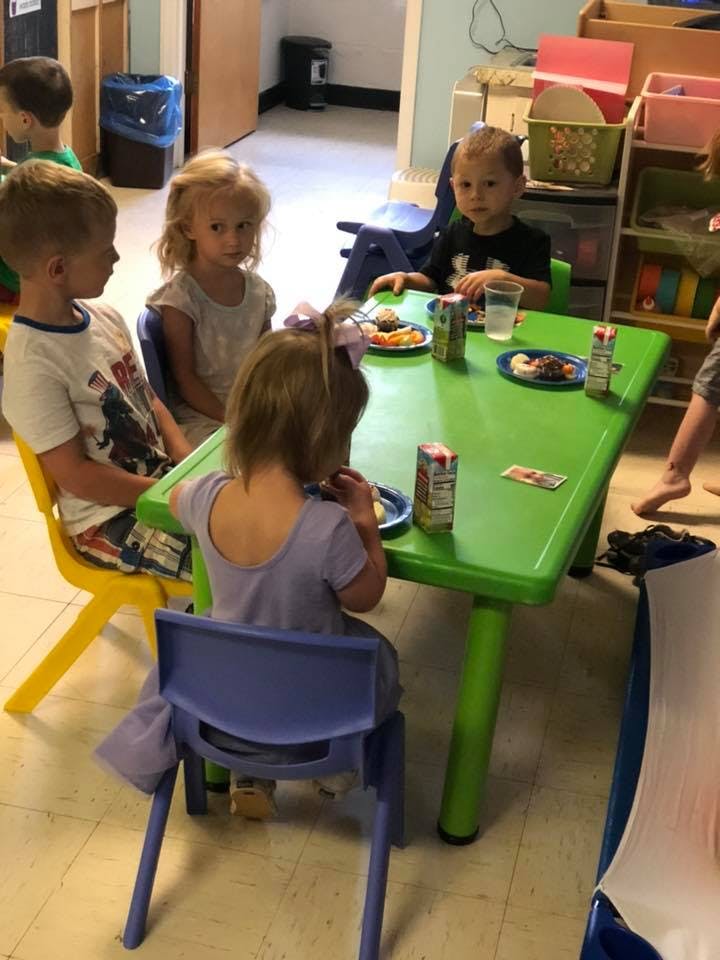 Children sitting at a green table with plates and drinks