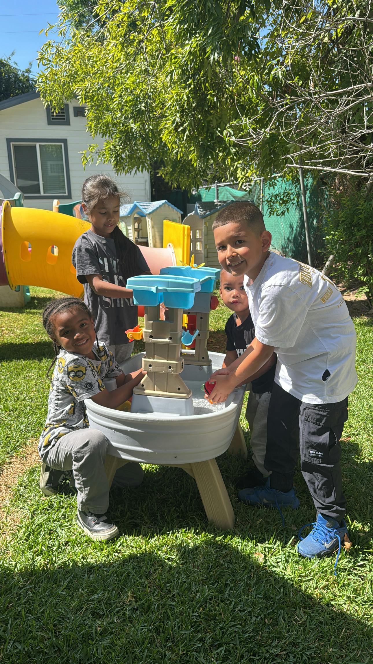 Four children playing with a water table in a grassy backyard