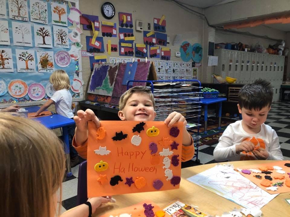 Child holding up a Halloween craft in a classroom