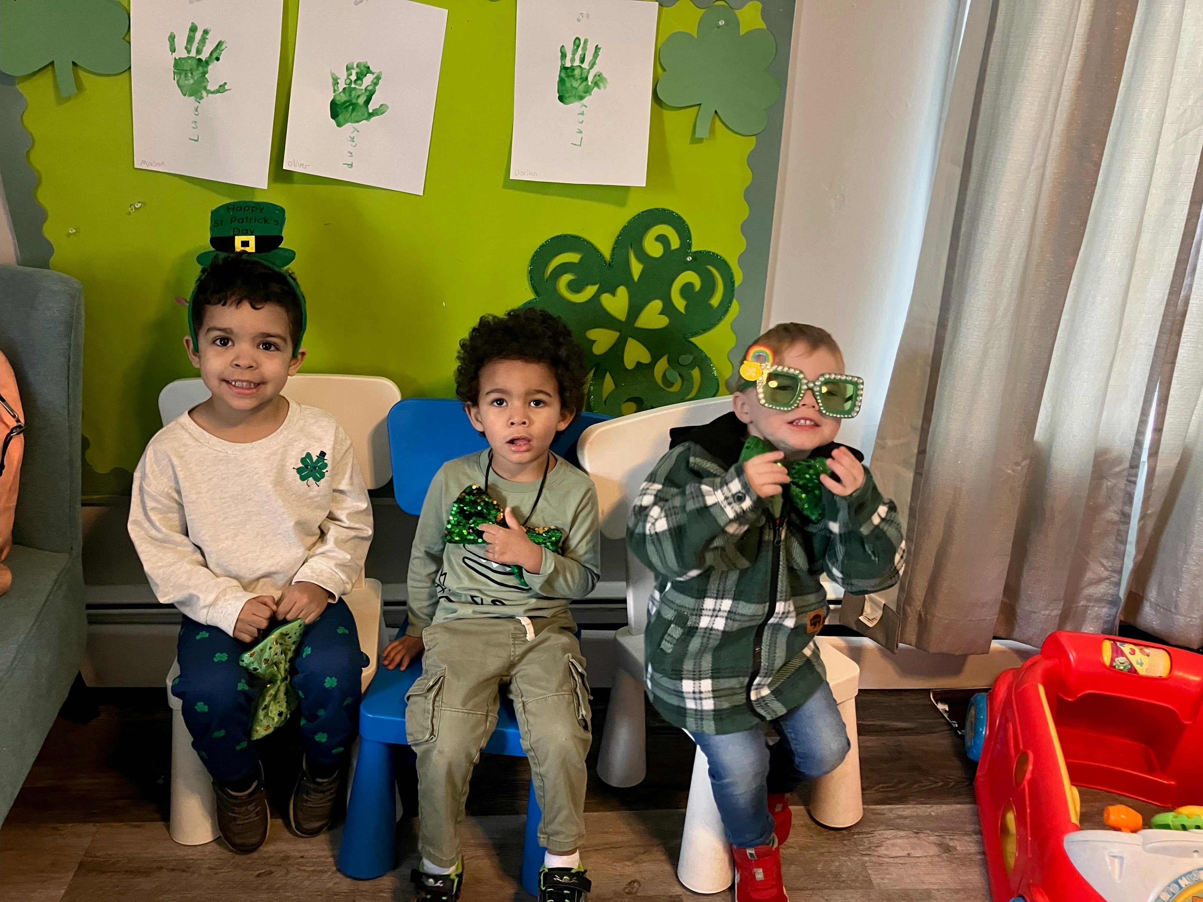 Three children sitting in chairs with St Patrick Day themed accessories