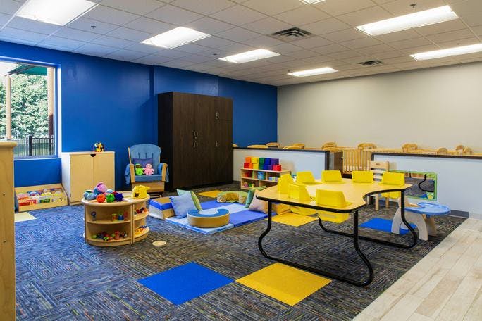Classroom with blue walls, yellow tables, and play mats