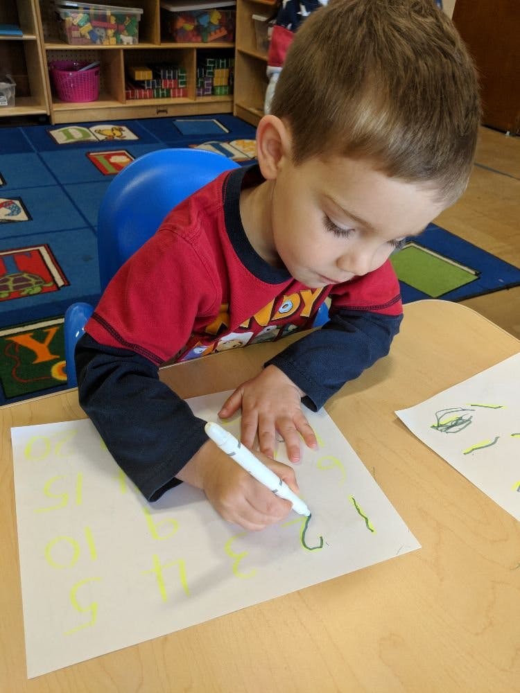 Child drawing on paper with a marker in a classroom