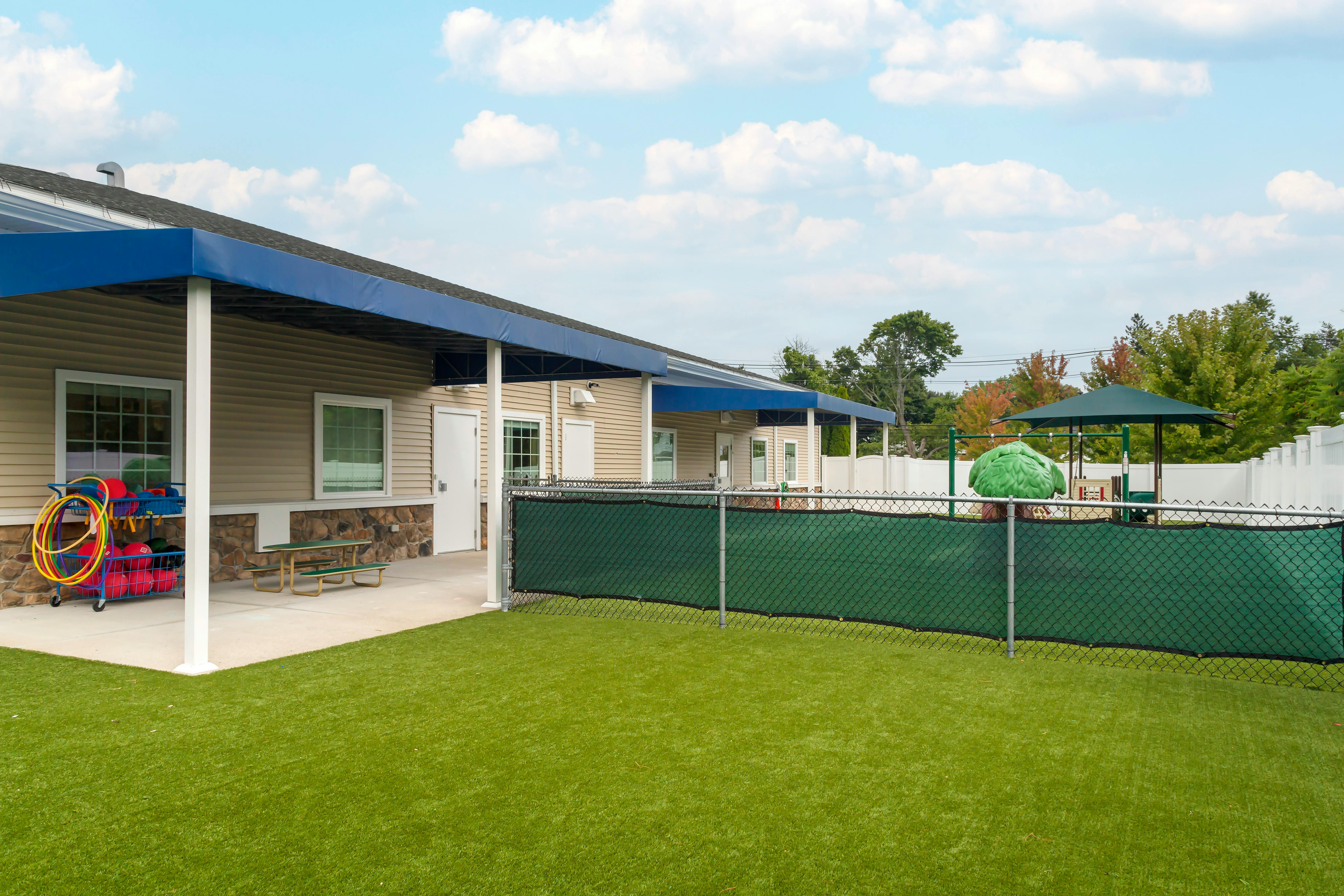 Outdoor play area with artificial grass and a building with a blue awning
