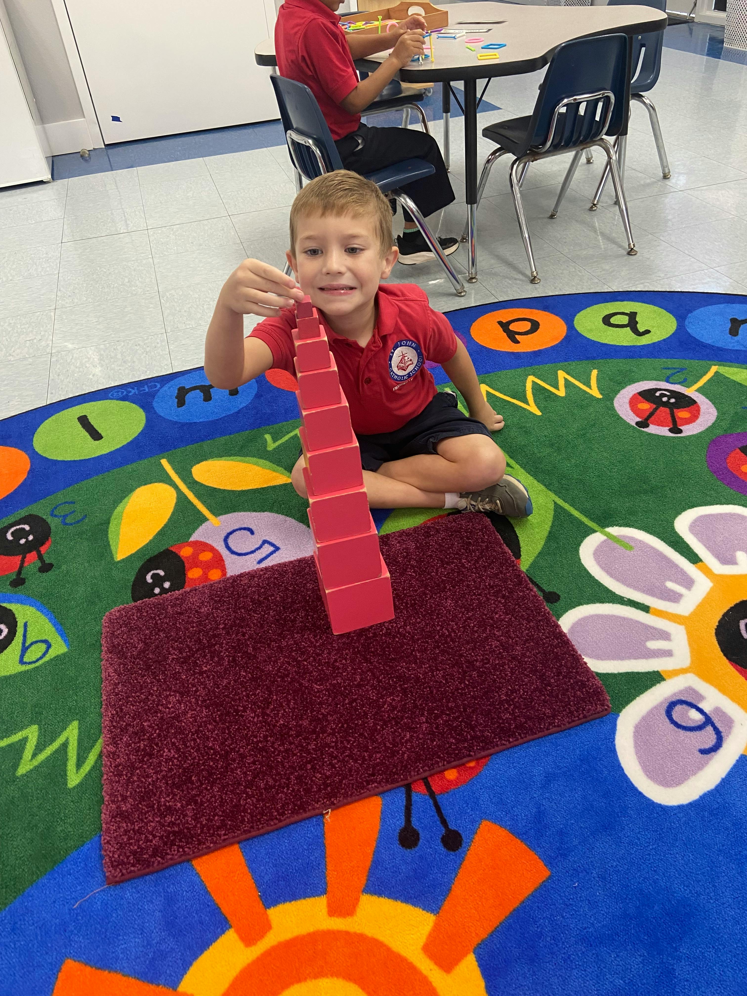 Child sitting on a rug holding a stack of red blocks