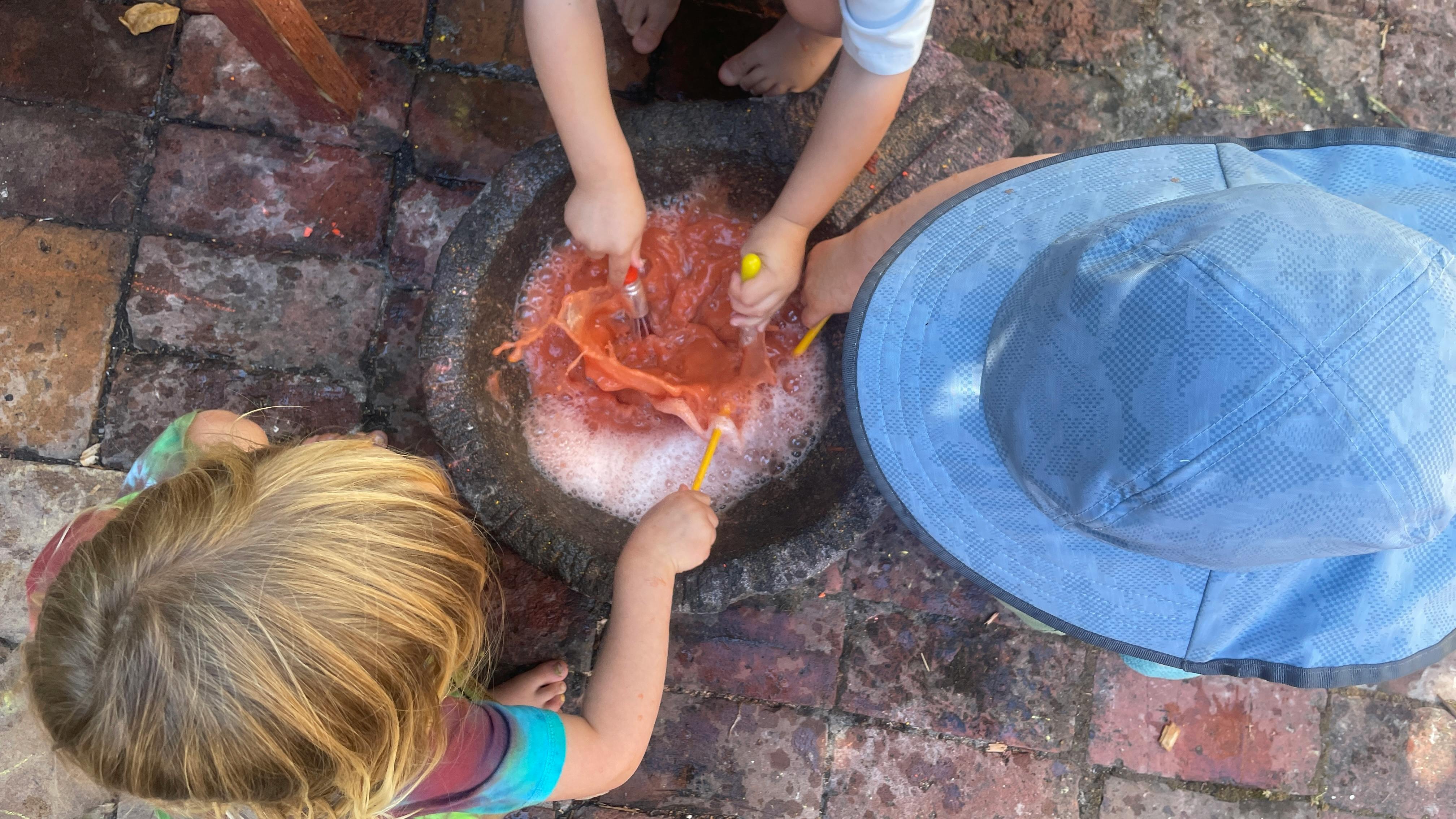 Children mixing orange liquid in a stone basin