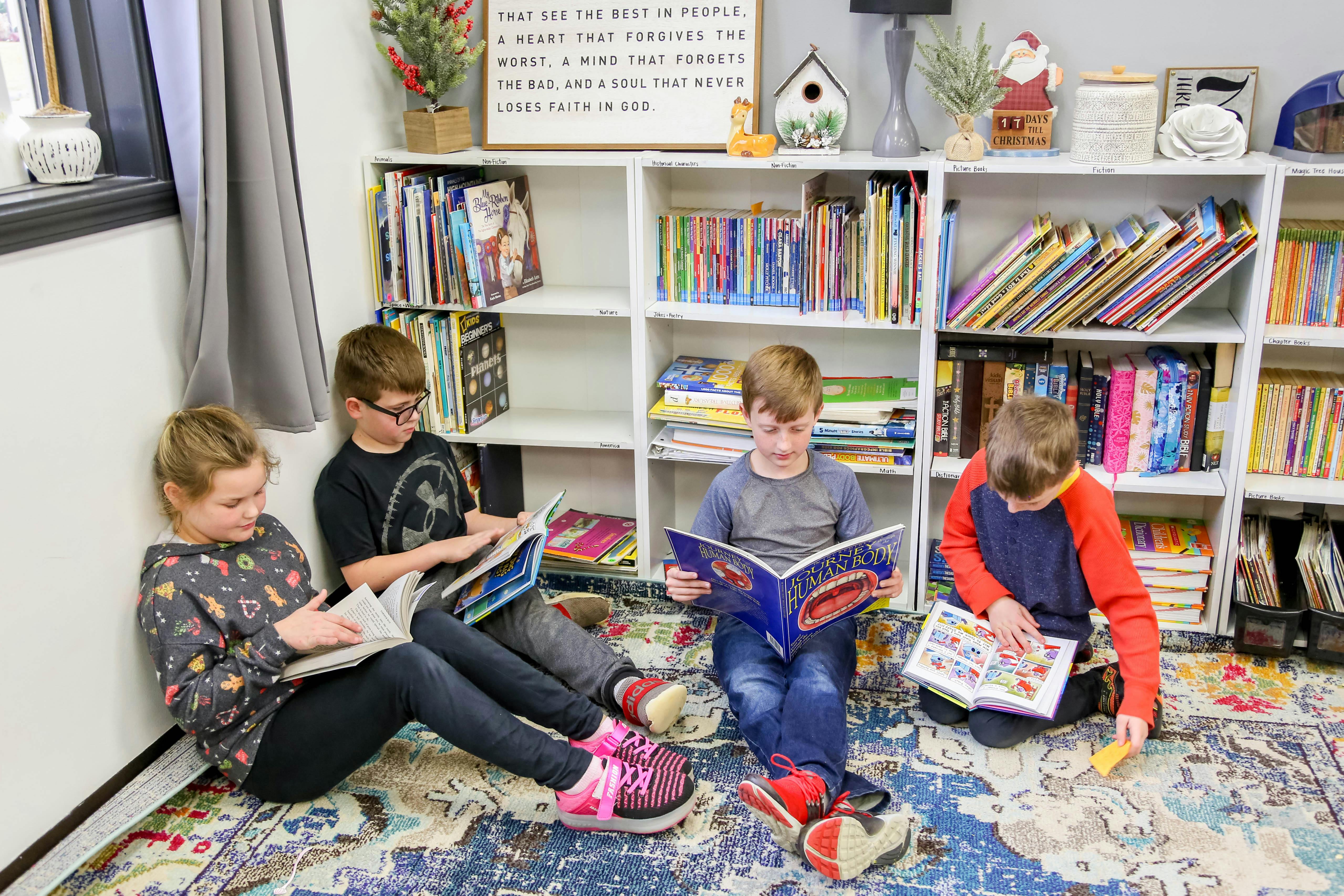 Three children reading books on the floor in a room with bookshelves