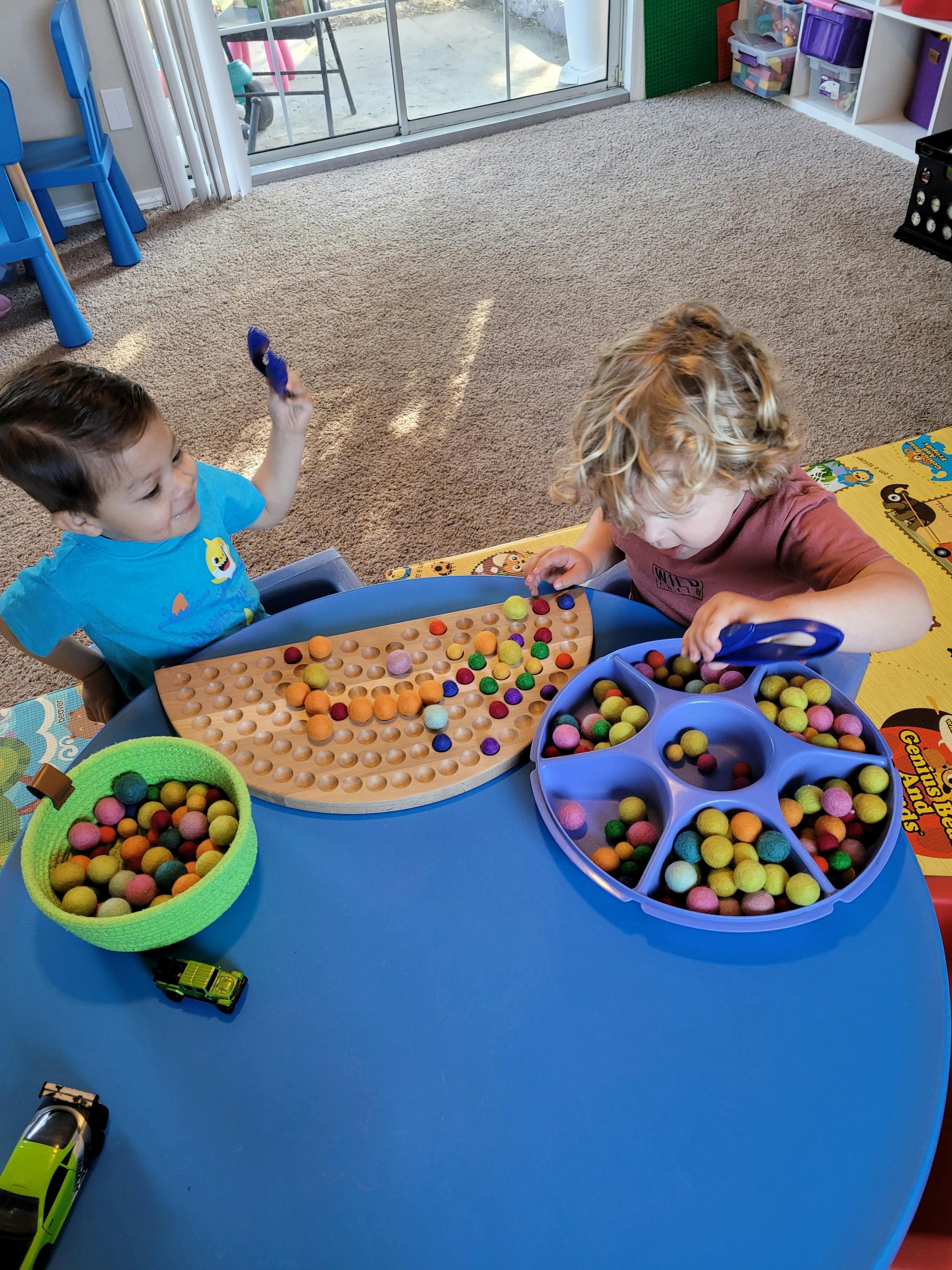 Two children playing with colorful beads and a pegboard on a blue table