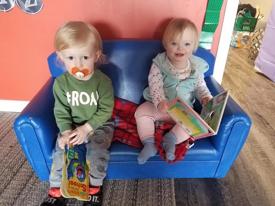 Two children sitting on a blue couch, one holding a book