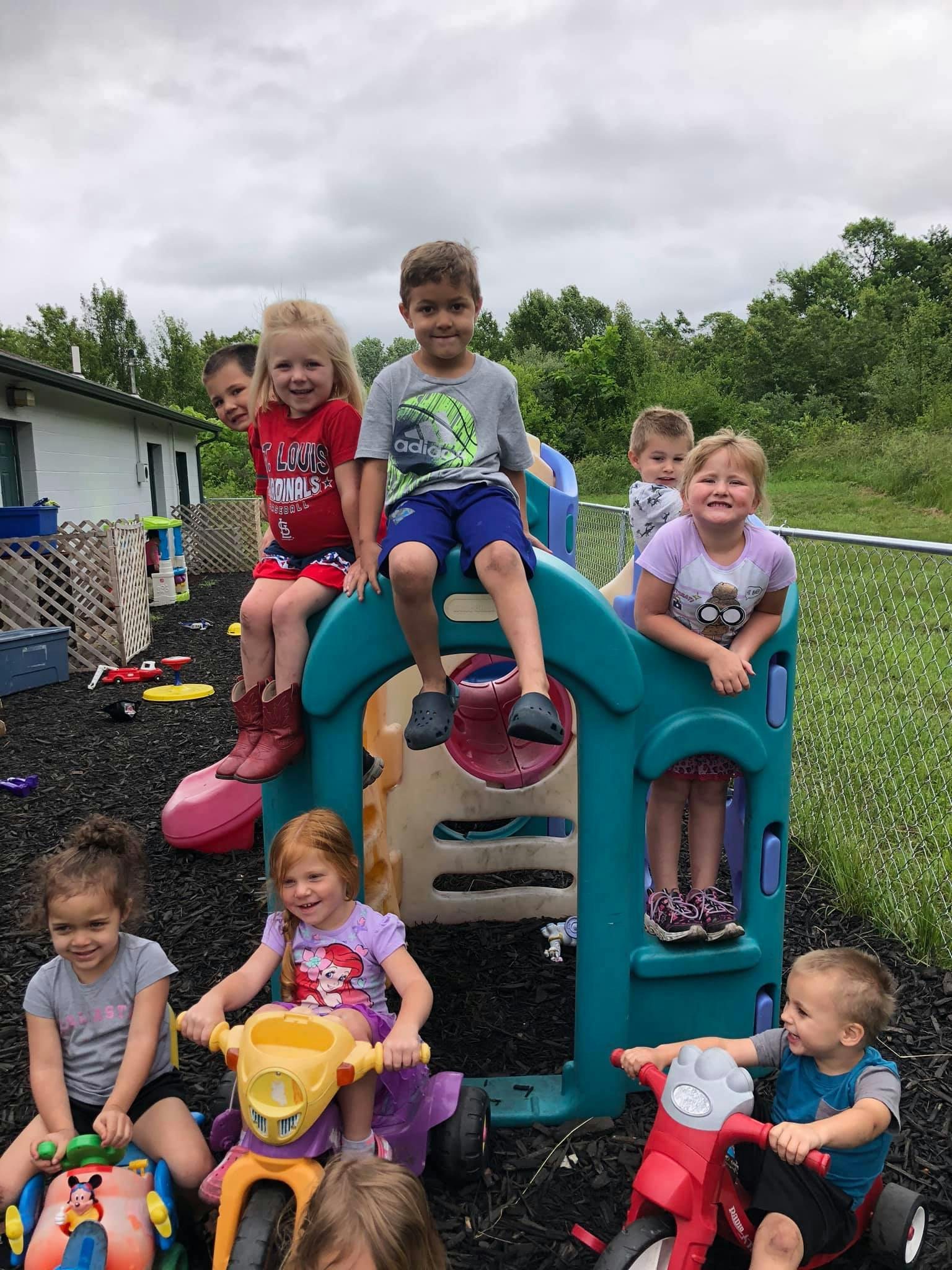 Children playing on a playground structure and riding tricycles outdoors